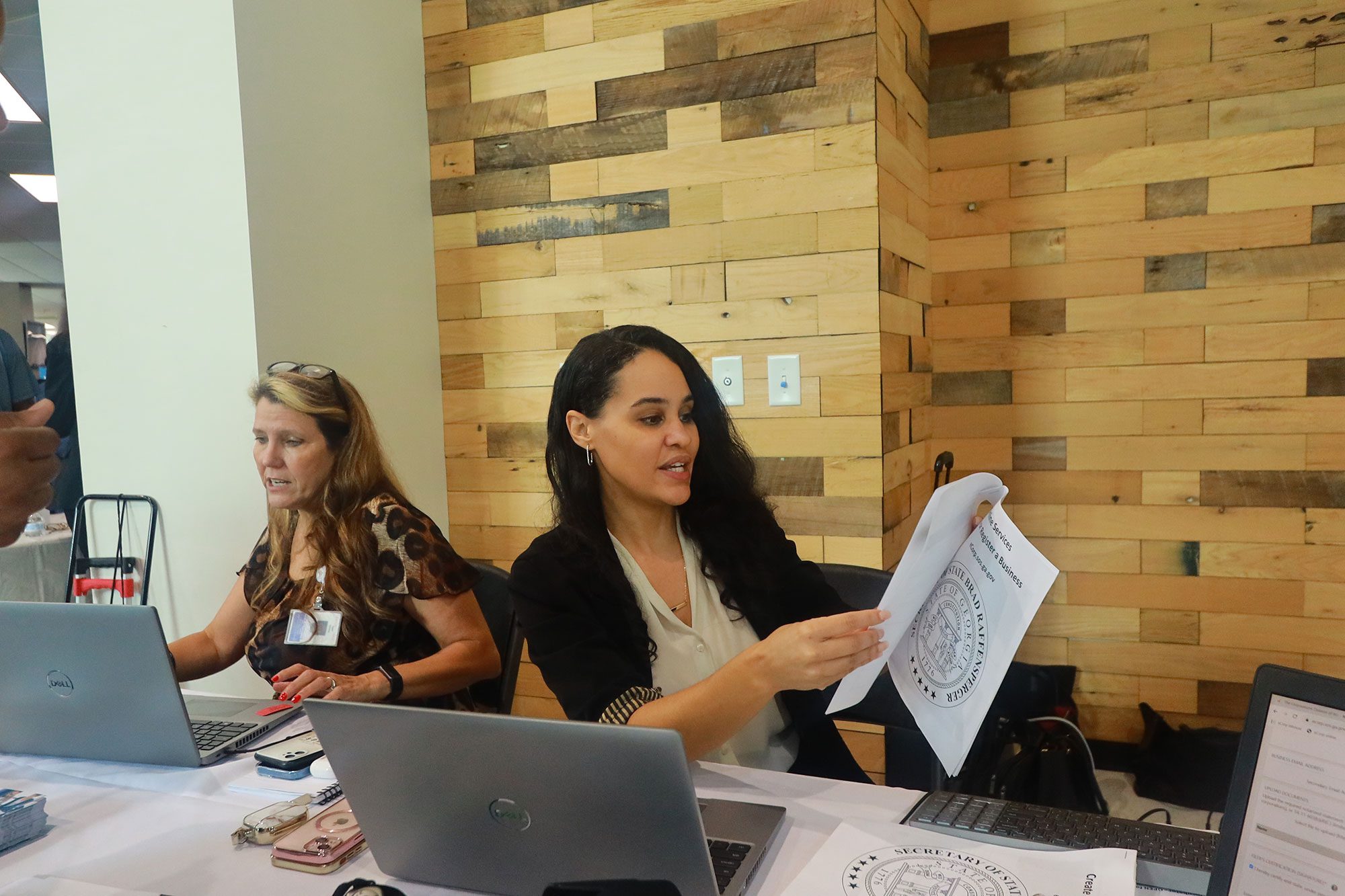 Two women working at a table. One holds a paper packet with instructions for registering a small business in Georgia.